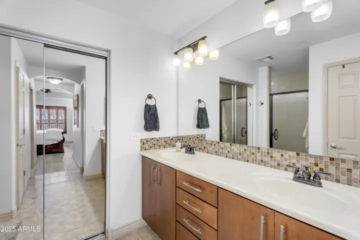 The primary bath offers dual sinks, mosaic backsplash, and generous cabinetry—adding function and flair to this updated lock-and-leave Phoenix residence.