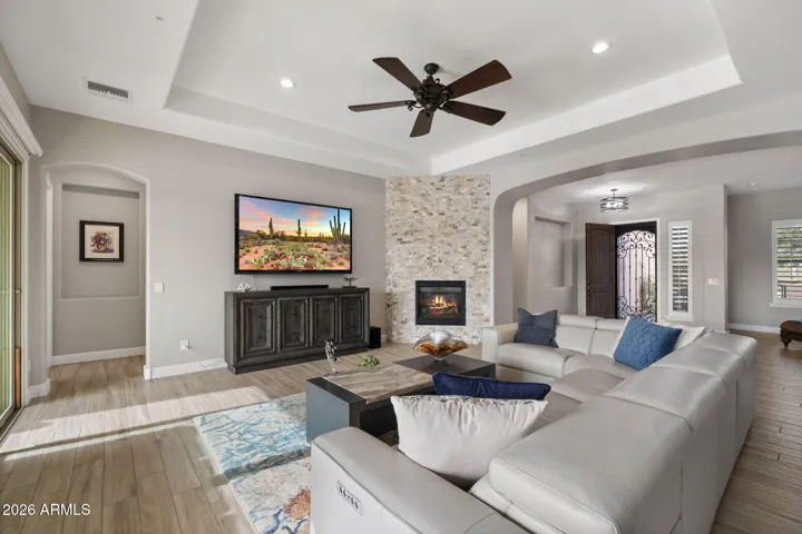 Elegant great room featuring stone-accent fireplace, tray ceiling, recessed lighting, and open-concept design ideal for entertaining.