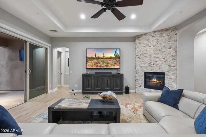 Great room featuring stone-accent fireplace, tray ceiling, ceiling fan, and open-concept layout perfect for entertaining.