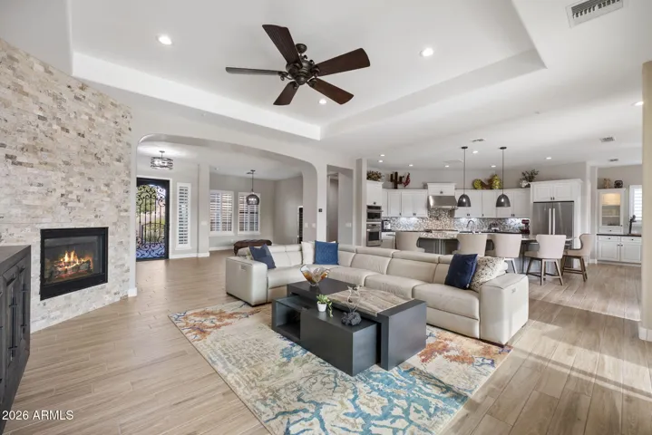 Open-concept great room with wood-look tile flooring, custom fireplace, and seamless flow to kitchen and living areas.