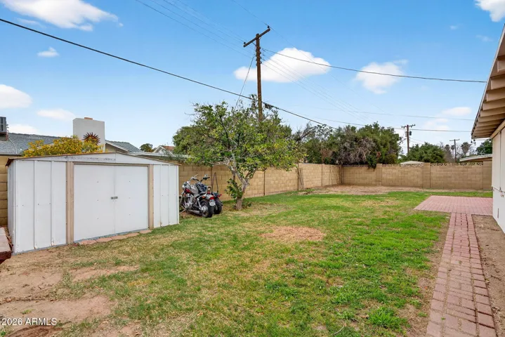 Large backyard featuring mature landscaping, block fencing, and a detached storage shed for added utility. The expansive lot provides flexibility for recreation, entertaining, or future improvements in this Phoenix residence.