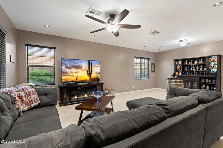 This spacious great room in Peoria features neutral tile flooring, recessed lighting, and a ceiling fan for added comfort and energy efficiency. A modern electric fireplace with media center creates a warm focal point, while the open layout flows seamlessly into the kitchen and dining areas—ideal for entertaining.