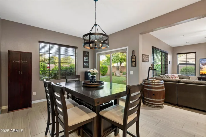 The open-concept dining and kitchen area offers seamless flow for entertaining in this Peoria home. Large windows provide natural light, while neutral tile flooring, updated lighting fixtures, and easy access to the backyard patio enhance both comfort and energy efficiency.