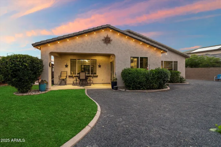 The rear exterior highlights charming string lights, a covered patio, and low-maintenance landscaping. This Peoria home blends curb appeal with functional outdoor living space, perfect for relaxing evenings.