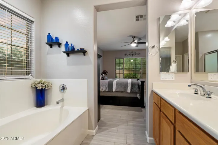 Enjoy a relaxing soaking tub and separate glass-enclosed shower in the spacious primary bath. Dual vanities, ample cabinetry, and modern lighting enhance both convenience and style in this Peoria home.