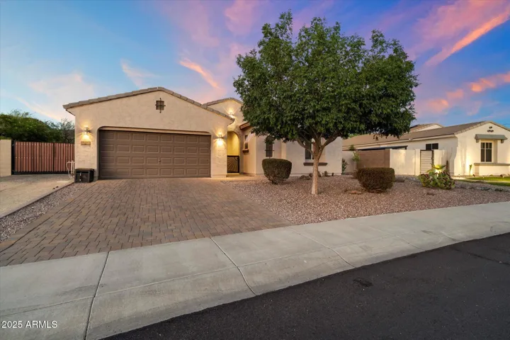 Twilight photography highlights the welcoming exterior of this Peoria property, featuring a paver driveway, desert landscaping, and an arched entryway. Exterior lighting adds warmth and security while enhancing the home's architectural character.