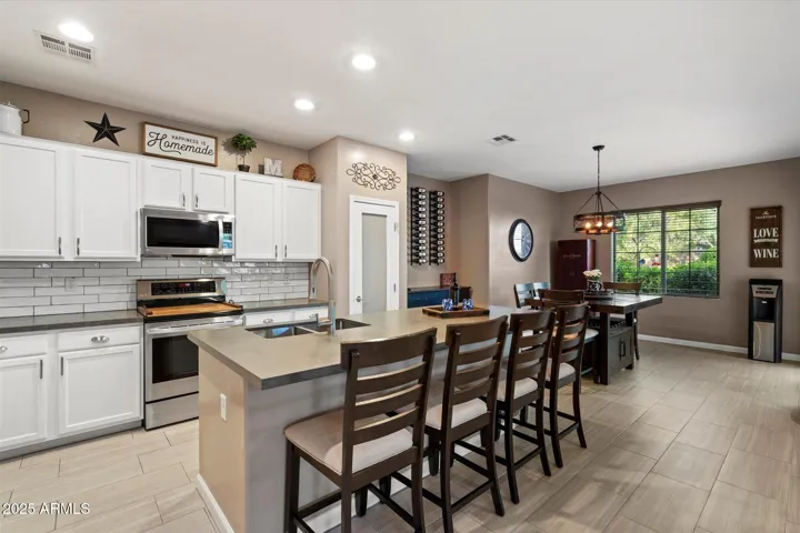 The updated kitchen in this Peoria home features white cabinetry, stainless steel appliances, subway tile backsplash, and a spacious breakfast bar with seating. Modern lighting and energy-efficient fixtures enhance both functionality and style in this beautifully maintained space.