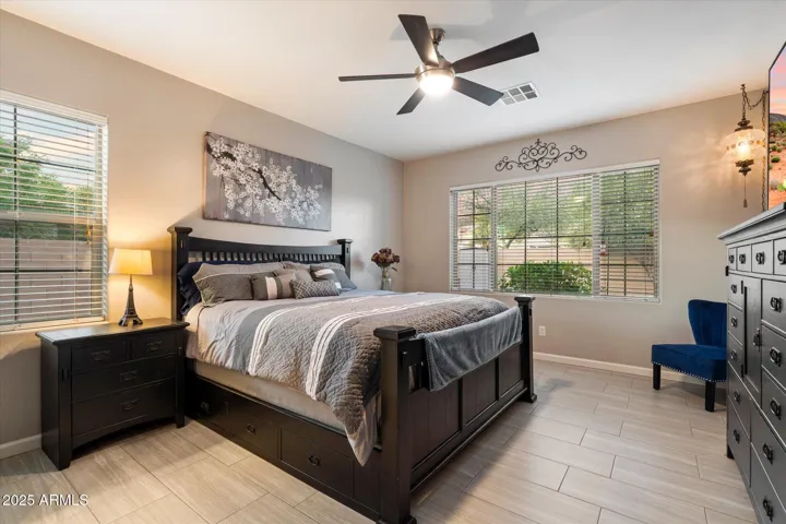 The primary bedroom in this Peoria home offers generous space, neutral tile flooring, ceiling fan, and large windows overlooking the backyard. Designed for comfort and energy efficiency, this private retreat provides a relaxing atmosphere with modern finishes.