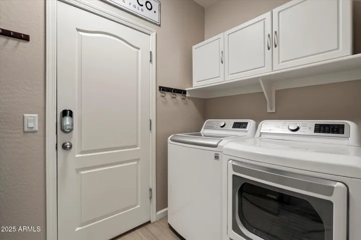 The interior laundry room includes upper cabinetry for storage, modern washer and dryer, and convenient access to the garage. Designed for efficiency and organization, this feature adds practical value to this Peoria home.