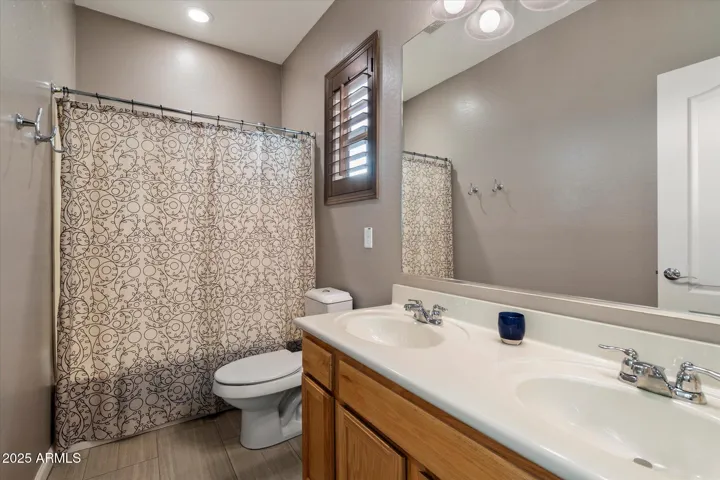 The secondary bathroom includes dual sinks, ample counter space, and a full shower-tub combination. Neutral tones and updated lighting maintain consistency with the modern finishes found throughout this Peoria home.