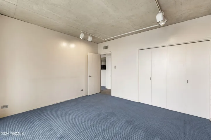 Bedroom retreat featuring generous closet space and clean, loft-style lines with exposed concrete ceiling above.