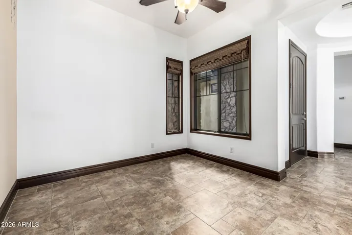 Light-filled living area with large windows, tile flooring, and ceiling fan. This versatile space in the Goodyear home is perfect for relaxing, entertaining, or creating a formal sitting area.