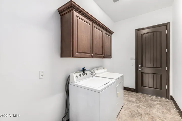 Bright laundry room in Goodyear featuring washer and dryer setup, overhead cabinetry, and tile flooring. Designed for convenience with ample storage and efficient layout for daily tasks.