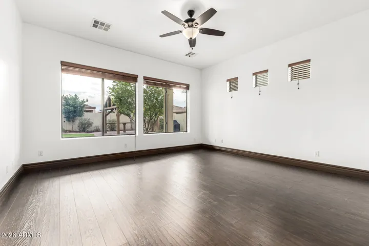 Large bedroom featuring wood flooring, ceiling fan, and natural light from multiple windows. This Goodyear home offers comfortable and versatile living spaces for relaxation.