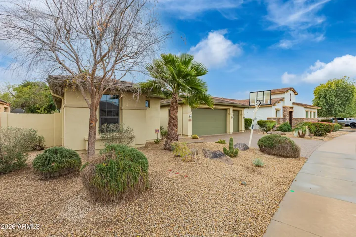 Side exterior view featuring desert landscaping, mature plants, and clean stucco finishes. This Goodyear home offers low-maintenance outdoor spaces with attractive curb appeal from multiple angles.