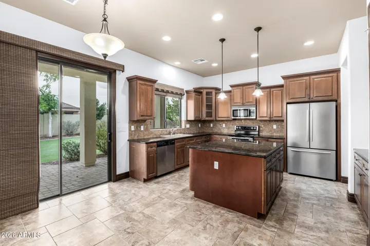 Gourmet kitchen featuring granite counters, stainless steel appliances, and sliding door access to the backyard. This Goodyear home blends indoor comfort with outdoor living convenience.