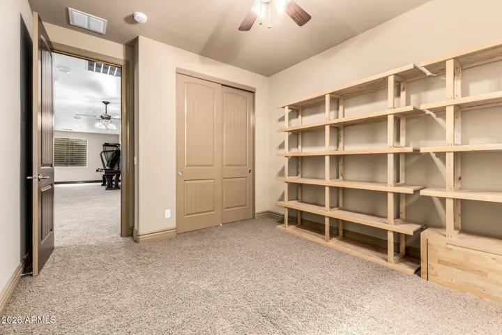 Versatile flex room in Goodyear featuring custom built-in shelving, plush carpet, and neutral tones—perfect for a home office, hobby space, or additional storage. Thoughtfully designed with ample organization and modern finishes.