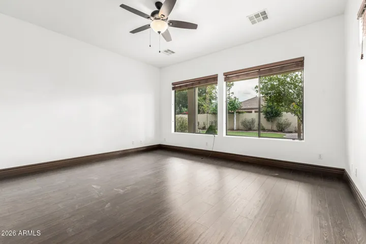 Generously sized bedroom in Goodyear with large windows showcasing backyard views, wood flooring, ceiling fan, and abundant natural light—perfect for comfort and relaxation.