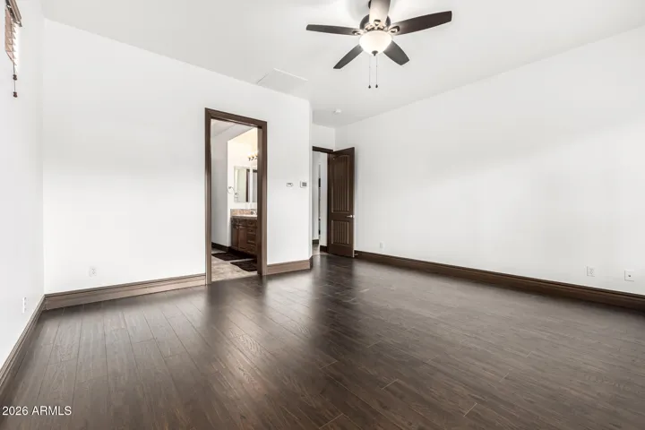 Bright and spacious primary bedroom in Goodyear featuring rich wood flooring, neutral paint, ceiling fan, and private access to the ensuite bathroom—an inviting retreat with modern updates and ample natural light.