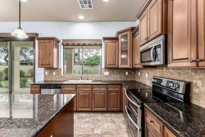 Light-filled kitchen with expansive window over the sink, granite counters, and stainless appliances. This Goodyear home offers a welcoming and functional cooking space.