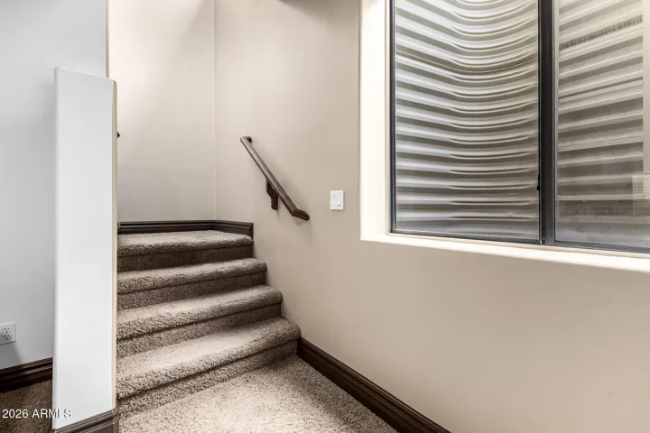 Interior staircase in this Goodyear property showcasing plush carpeting, wood handrail, and natural light from nearby window. A well-maintained and stylish transition between levels with updated finishes.