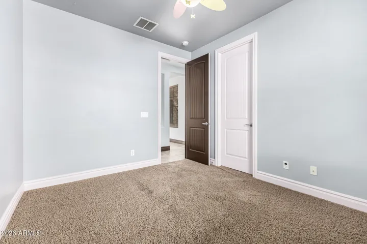Generous bedroom space featuring upgraded carpet, ceiling fan, and dual-door access for added convenience. Located in a Goodyear home, this room offers flexibility for guests, office use, or everyday living.