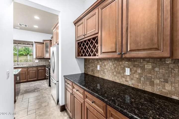 Elegant butler’s pantry with granite countertops, custom maple cabinetry, and built-in wine rack. This functional space enhances the gourmet kitchen in this Goodyear home, perfect for entertaining and additional storage.