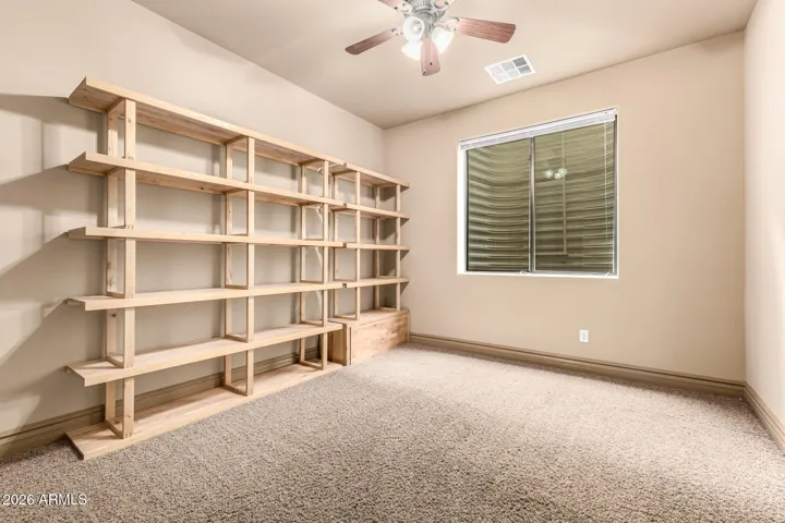 Unique bedroom space with custom wood shelving system, plush carpet, and natural light. Ideal for storage or creative use, this Goodyear room blends functionality with thoughtful design.