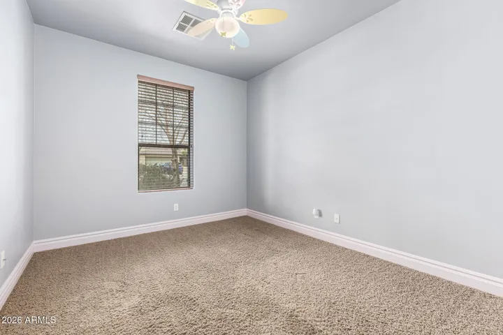 Inviting bedroom in Goodyear with plush carpet, soft neutral tones, and a large window providing natural light. Ceiling fan adds energy efficiency and comfort, creating a peaceful retreat with modern updates.