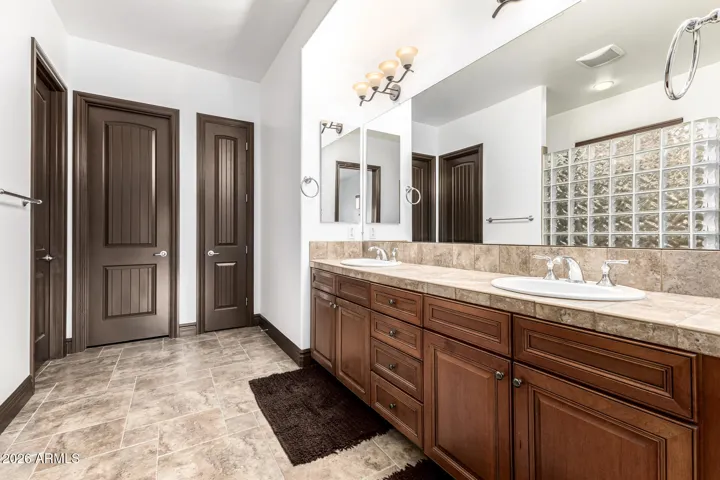 Elegant primary bathroom in Goodyear featuring a dual sink vanity, rich wood cabinetry, updated lighting, and tile flooring—designed for convenience and everyday luxury.