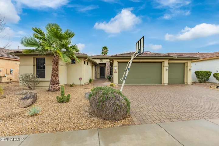 Daytime exterior view showcasing desert landscaping, palm trees, and a paver driveway leading to a 3-car garage. This Goodyear property offers strong curb appeal and a welcoming residential setting.