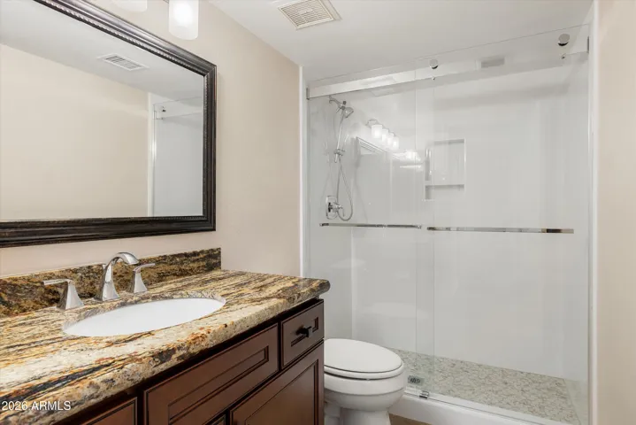 This bathroom has been updated with a walk-in shower with glass enclosure, granite counters, and cherry stained wood cabinetry.