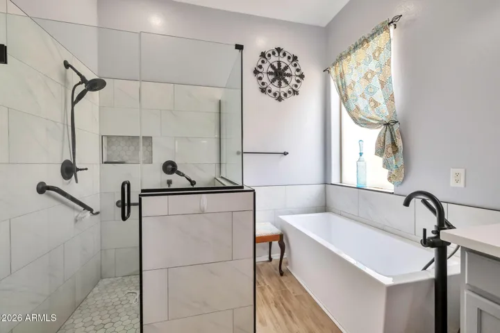 Bright and modern primary bath showcasing a custom tiled walk-in shower with glass enclosure and a relaxing soaking tub. Neutral tones and updated finishes enhance the home's comfort and appeal.