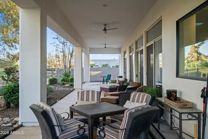 Scottsdale backyard featuring an expansive covered patio with multiple seating areas, ceiling fans, and sliding glass access. Ideal for indoor-outdoor living and entertaining near the pool and landscaped yard.