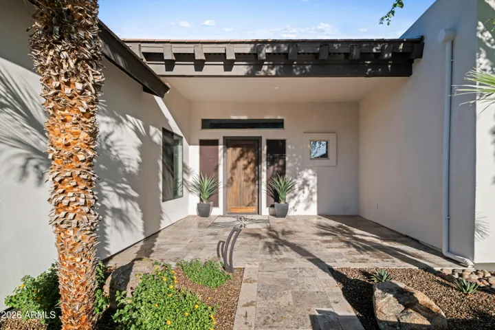 Elegant Scottsdale entry patio with travertine flooring, covered seating area, and desert landscaping. This inviting outdoor space enhances curb appeal and creates a warm welcome.