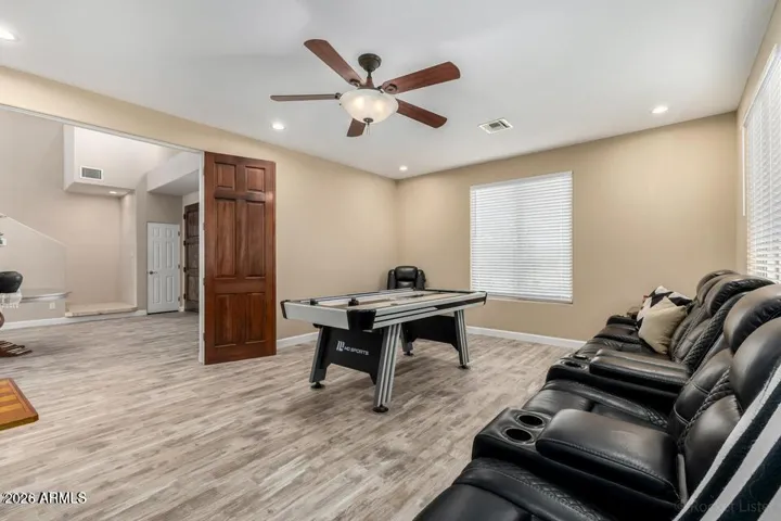 Spacious game room featuring an air hockey table, theater-style reclining seating, and abundant natural light—perfect for entertaining or relaxing.