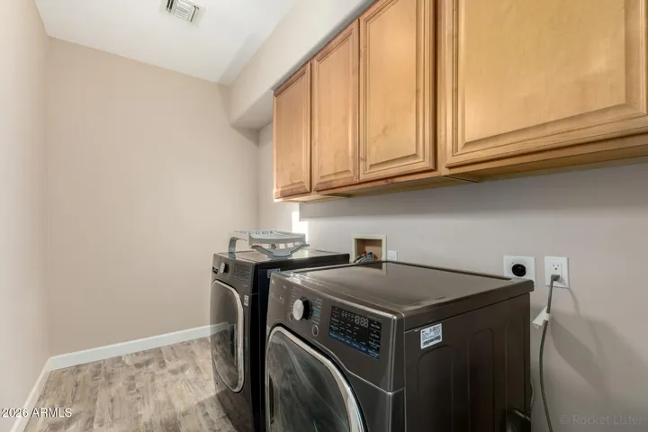 Dedicated laundry space with upper cabinetry and side-by-side washer and dryer.