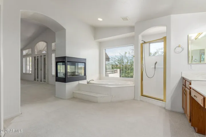 Dual sided gas fireplace next to step up sunken soaking tub in primary bathroom.