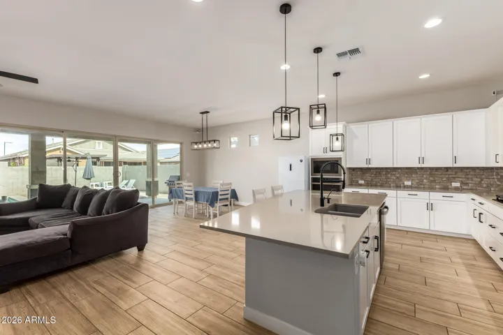Spacious open great room in this Surprise home featuring wood-look tile flooring, abundant natural light, and seamless flow to the backyard and dining area—perfect for modern living and entertaining.