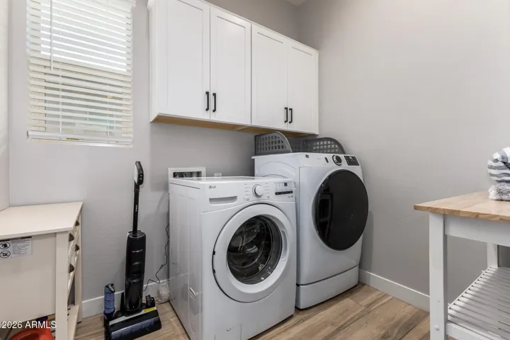 Functional laundry room with washer and dryer, upper cabinets, and natural light, enhancing everyday convenience in this Surprise home.