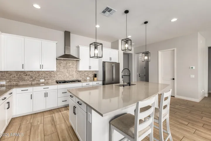 Stylish gourmet kitchen featuring quartz countertops, white shaker cabinets, stainless steel appliances, gas cooktop, and designer lighting in this Surprise home.