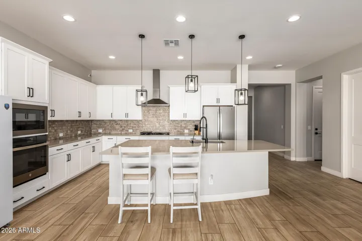 Gourmet kitchen with oversized island, pendant lighting, stainless appliances, and open layout connecting seamlessly to the living space in this Surprise home.