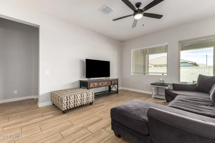 Comfortable living area featuring wood-look tile floors, ceiling fan, and direct access to the covered patio and pool, enhancing indoor-outdoor living in Surprise.