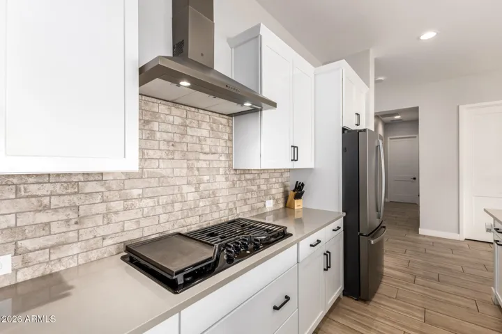 Modern kitchen in this Surprise home featuring gas cooktop, stainless hood, quartz countertops, and stylish stone backsplash with white shaker cabinets and upgraded finishes.