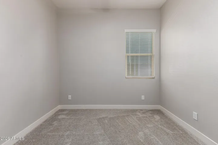 Comfortable bedroom with plush carpeting, natural light, and neutral finishes, offering flexibility for guests or a home office in this Surprise property.