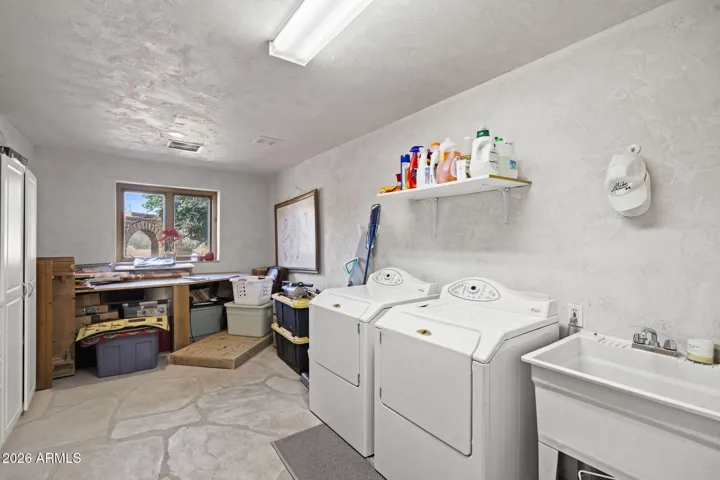 Functional laundry room featuring side-by-side washer and dryer, utility sink, built-in shelving, and generous workspace with natural light from the window.