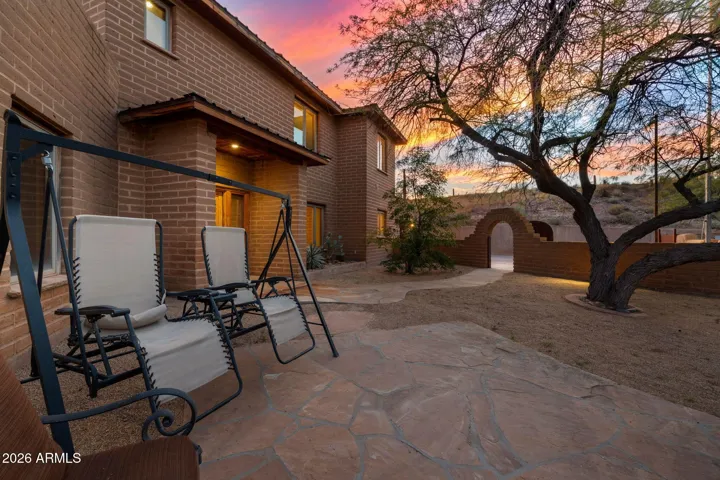 Front elevation highlighted by glowing interior lights and dramatic desert sunset skies, emphasizing architectural character and privacy wall.