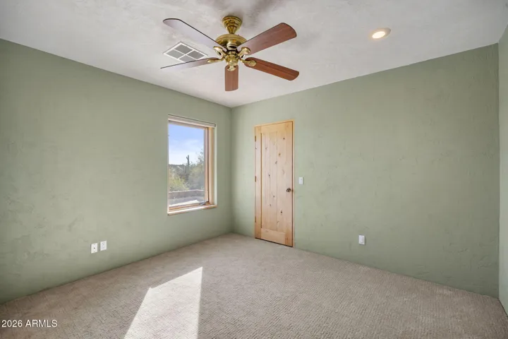 Bright secondary bedroom with carpeting, ceiling fan, and large window framing desert views.