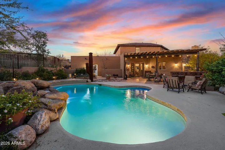Resort-style backyard featuring a freeform pool with natural rock accents, expansive patio space, and a covered pergola with built-in seating and ambient lighting, ideal for outdoor entertaining.