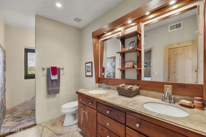 Spacious bathroom showcasing dual sinks, wood cabinetry, stone countertops, and a tiled walk-in shower.